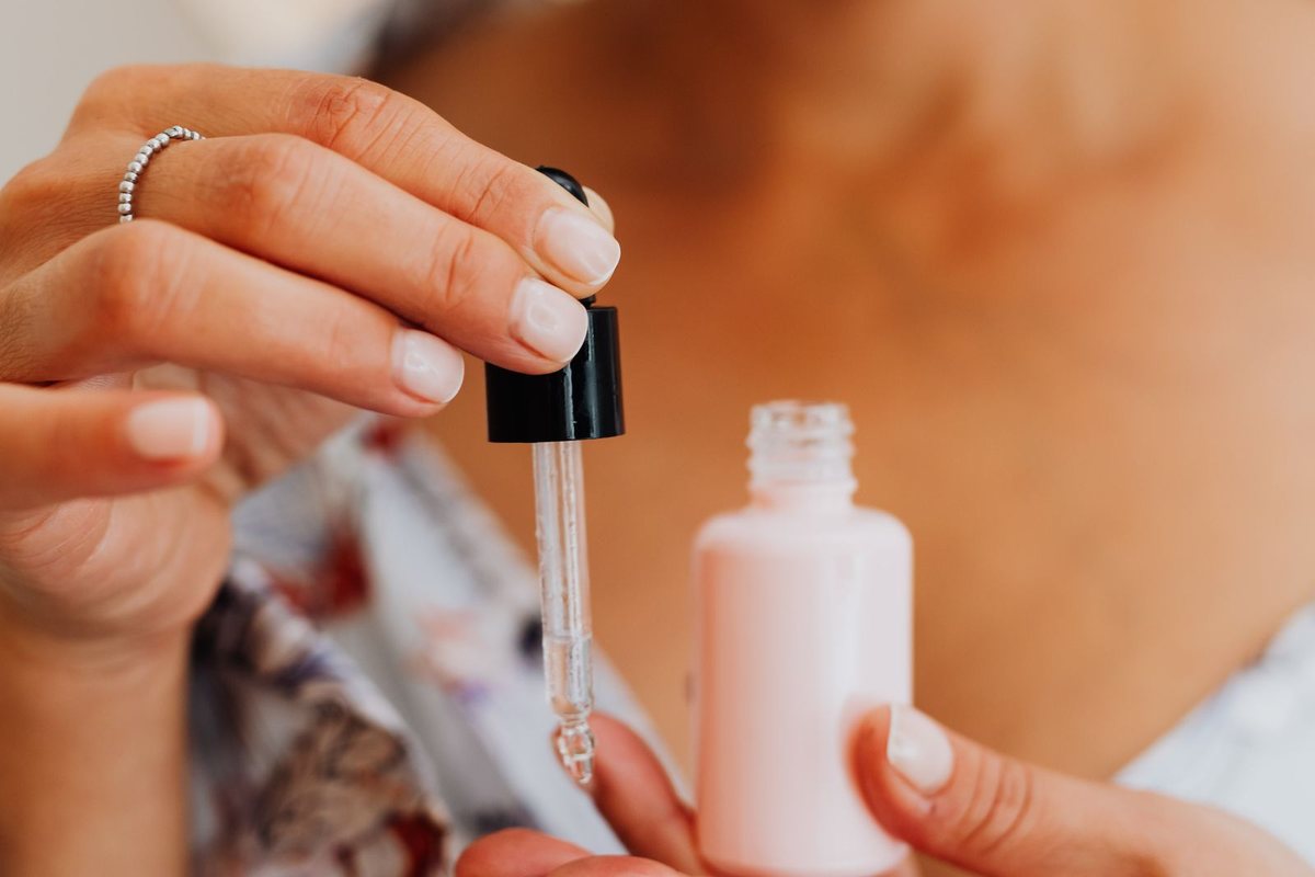 Close-up of a woman applying facial serum to her skin using a pipette dropper.