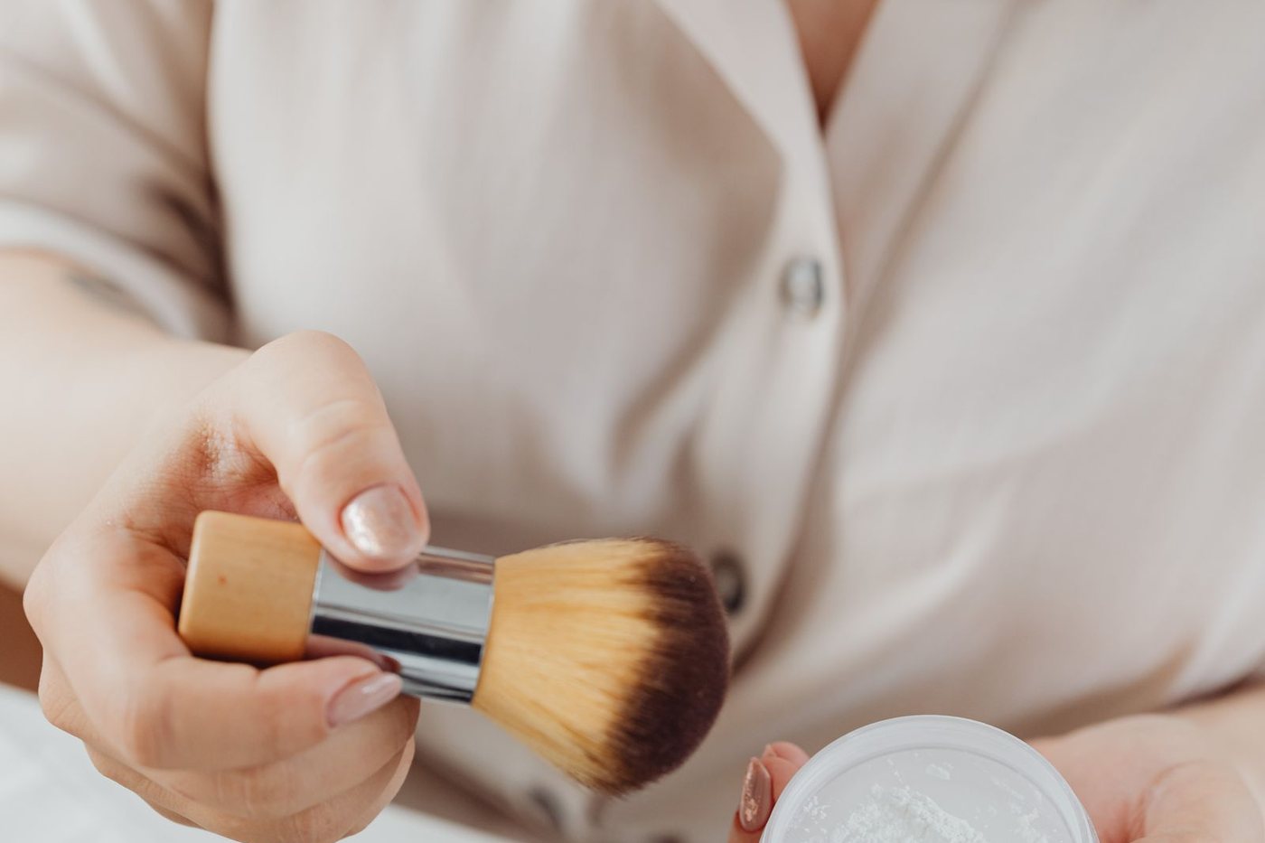 Close-up of a woman applying loose face powder with a large makeup brush.
